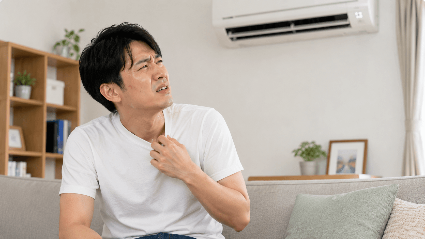 冷房が効かずに暑そうにする若い男性