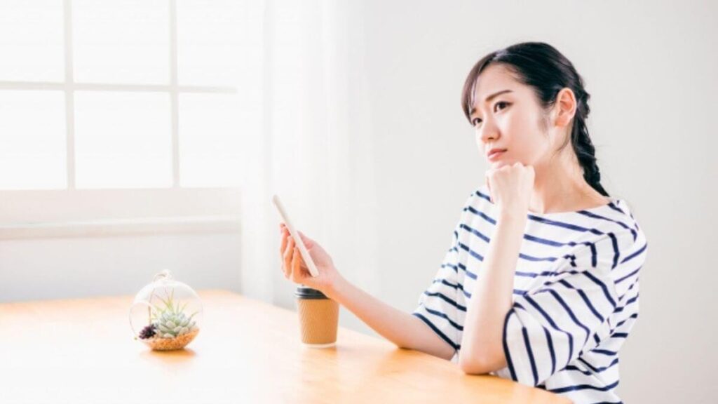 スマホを持ちながら考える若い女性